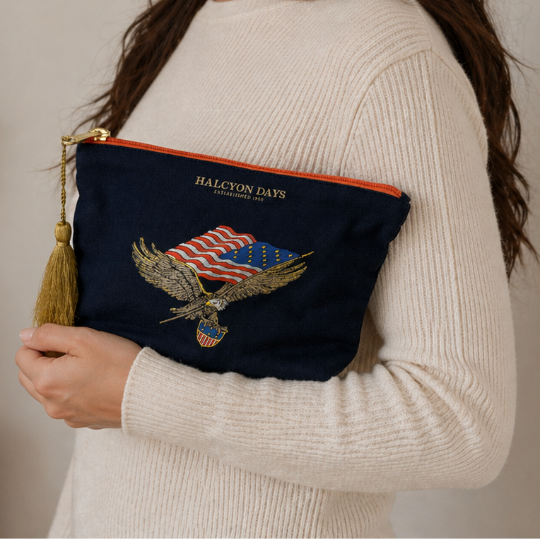 Woman holding a navy pouch with an eagle and flag design, wearing a white sweater.