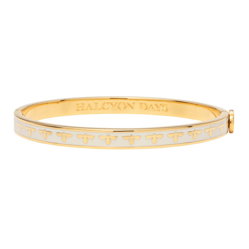 A gold bangle bracelet with a cream-colored bee design and enamel decoration.